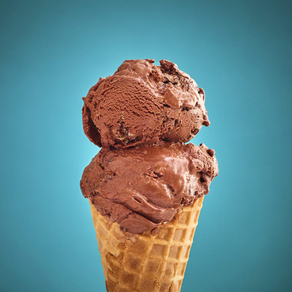 Double scoop of chocolate fudge brownie ice cream on a waffle cone with a blue background