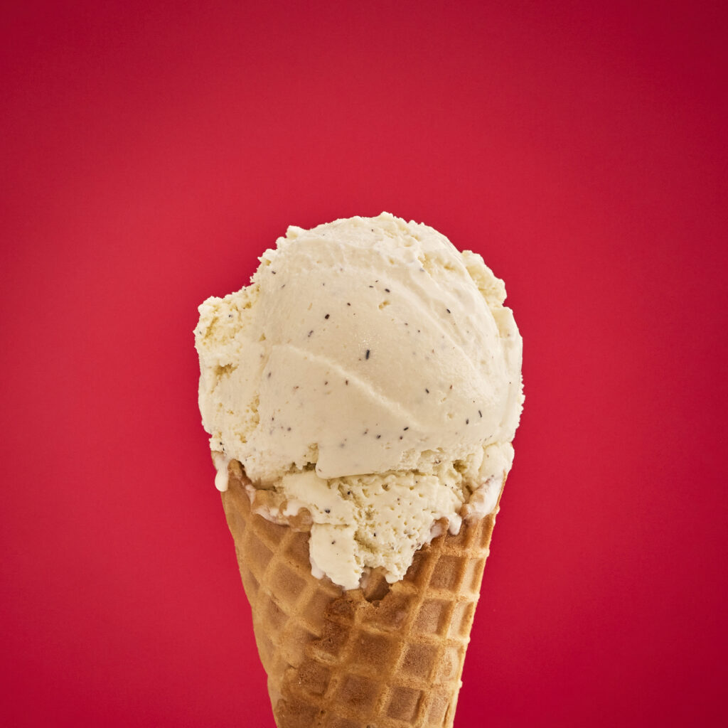 A double scoop of vanilla bean ice cream on a waffle cone in front of a red background
