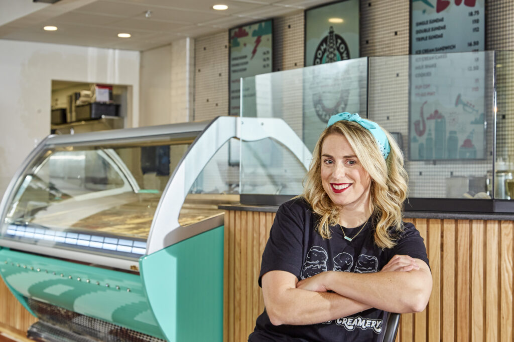 Photo of Angela Muir inside Boom Town Creamery, woman seated in front of ice cream case