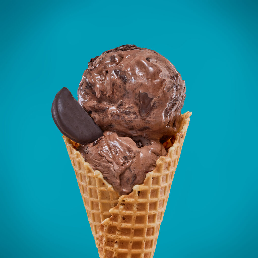 double scoop of Chocolate Mint ice cream  sitting on a waffle cone with a blue background
